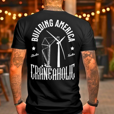 White man with tatoos wearing a black building america t shirt with renewable energy logo that is DTG printed on the back standing in a bar after a long day of working construction