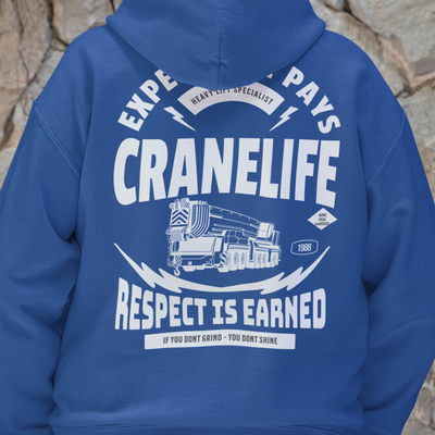 Navy blue crane operator hoodie on a man with his hands in his pockets against a cobble stone wall