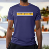 Black male with a blue craneaholic crane operator t shirt that has a DTG printed logo on the front that is white and yellow standing in a house with a white back ground