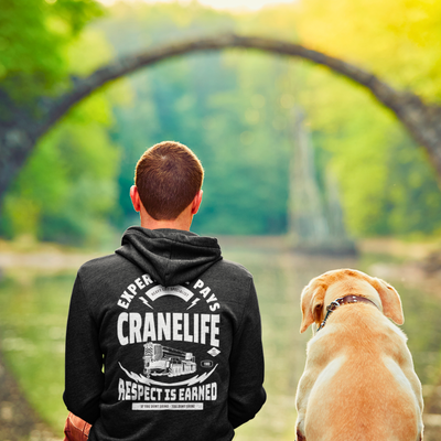 A man with brown hair and his yellow lab sitting by a lake wearing crane life hoodie in black