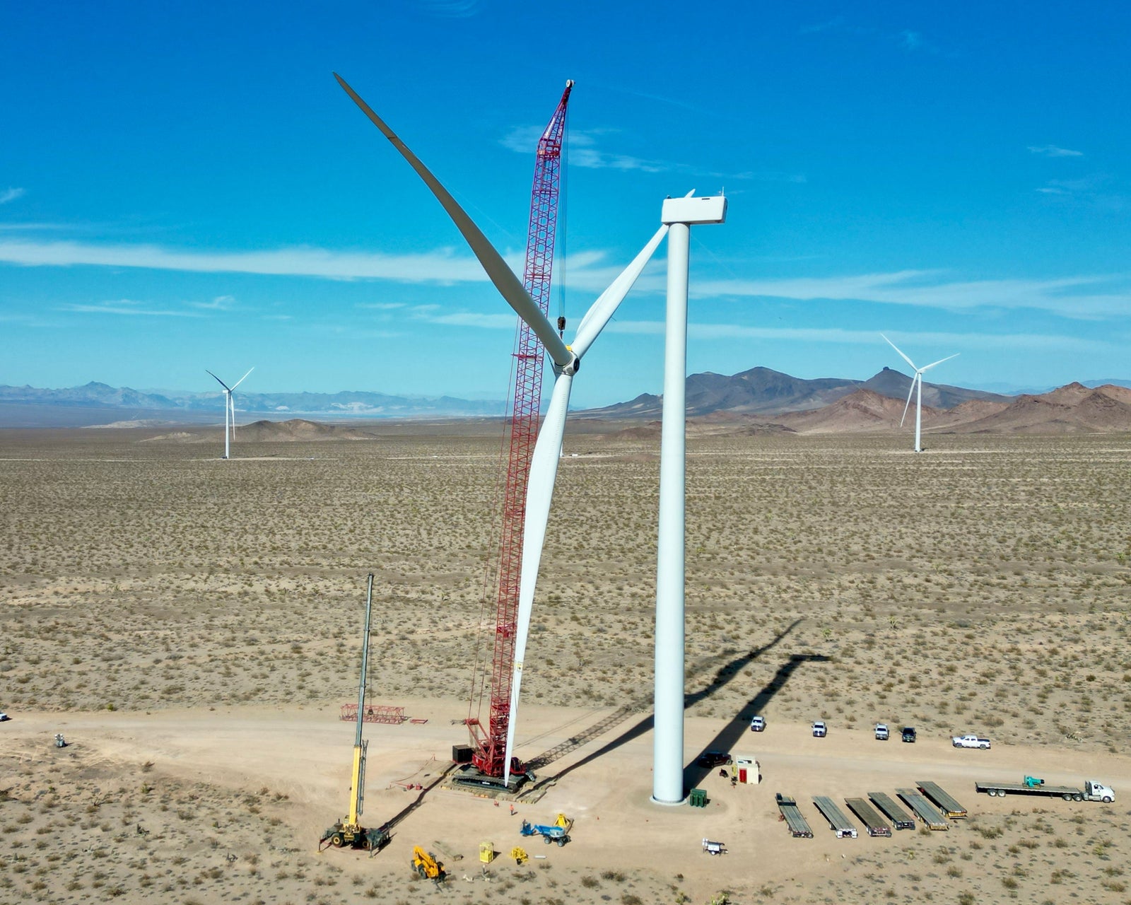 Wind turbine under construction in a desert landscape with mountains in the background.