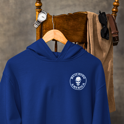 Navy blue bella canvas crane operator hoodie hanging on a mans chair with his watch belt and sunglasses after a long day at work at home showing a DTG printed design of building America on the front