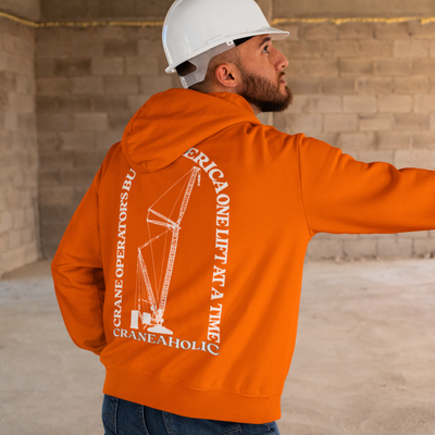 White male with brown beard on a construction site wearing a orange crane operator bella canvas hoodie with DTG design for crane operators printed on the back in white.