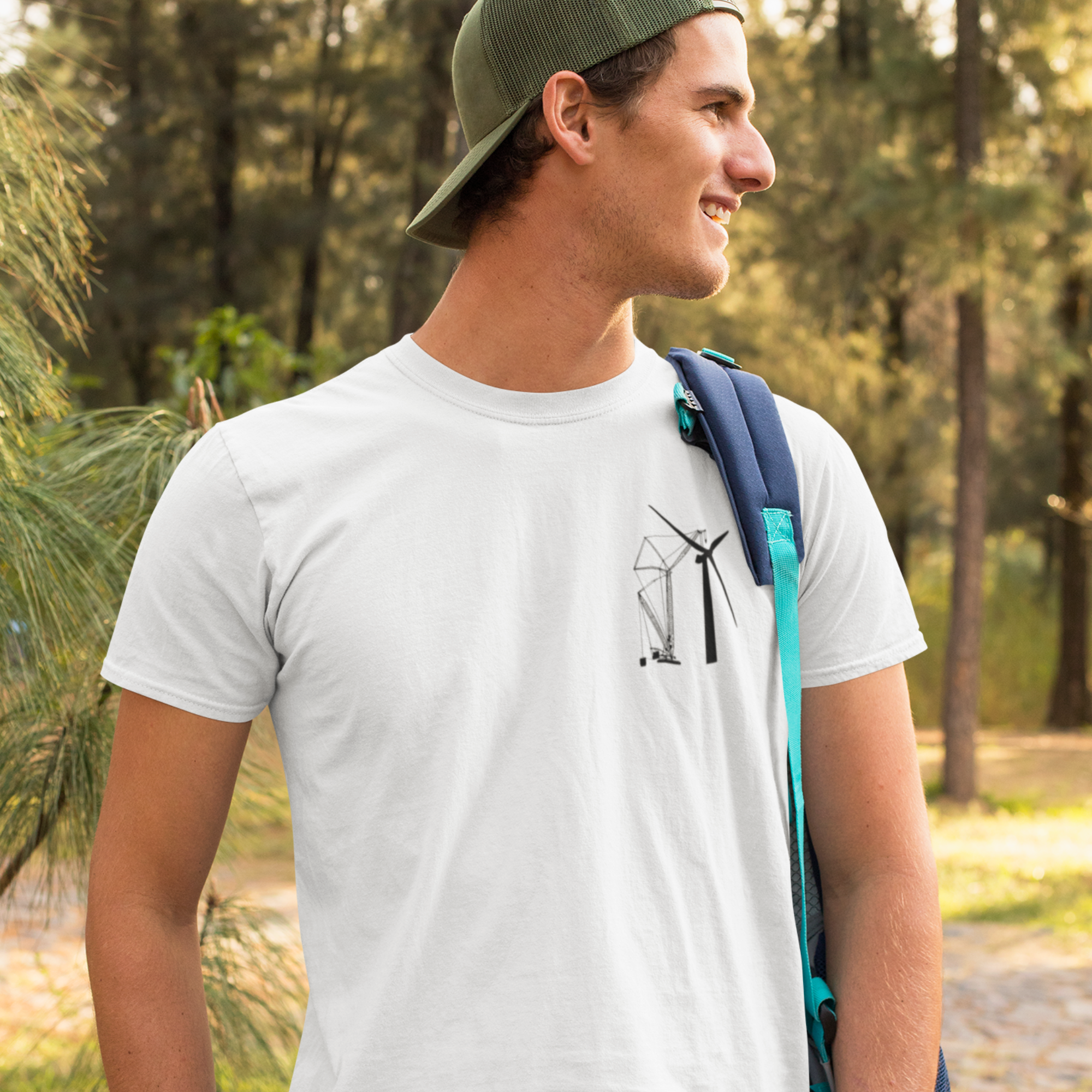 Clean shaved white male on a hike wearing a white t shirt with a DTG printed design of a crane building a wind turbine on the front of his shirt while in the woods